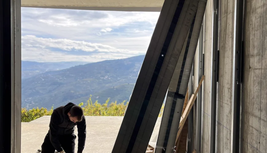 estaleiro de obra onde em primeiro plano se encontram materiais de obra e vemos um trabalhador e ao fundo uma paisagem sobr o rio douro