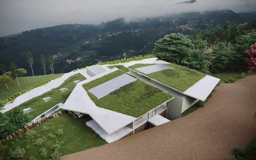 Vista aérea de uma estrutura moderna com telhados verdes e painéis solares, integrada na paisagem montanhosa. A arquitetura é minimalista, com grandes planos brancos e a relva no topo a mimetizar o ambiente circundante.