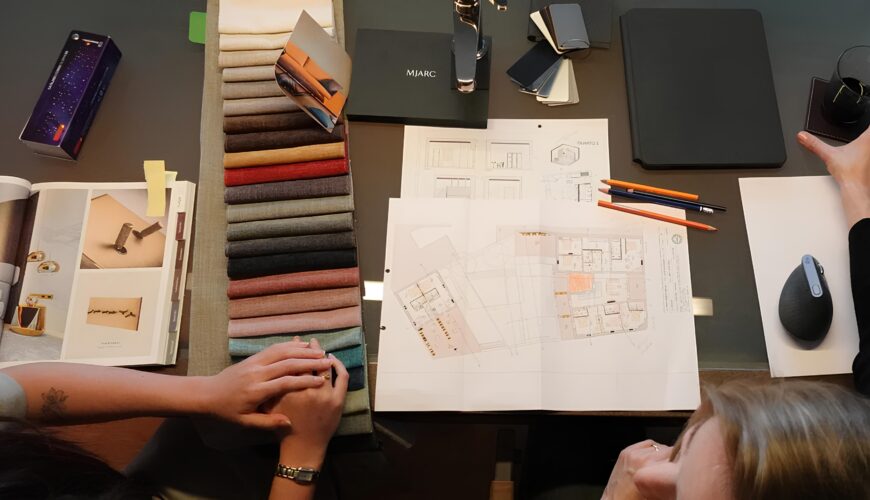 planos de arquitetura e diversas amostras de tecidos em cima de uma mesa, pisa papeis com logo da MJARC Arquitetos