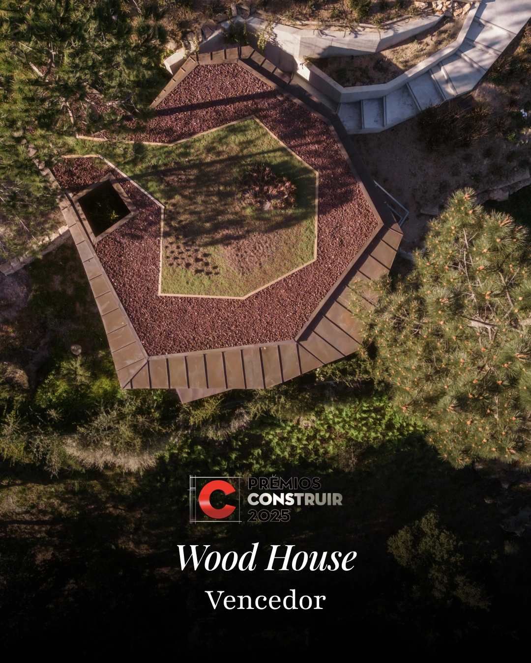 Vista aérea da 'Wood House', uma casa de arquitetura angular camuflada numa encosta arborizada. O telhado tem um desenho hexagonal com áreas cobertas de seixos vermelhos e uma área central relvada. Escadas de betão em segundo plano. Logótipo 'Prémios Construir 2023' sobreposto. O texto diz: 'Wood House | Prémio Sustentabilidade | Vencedor'.